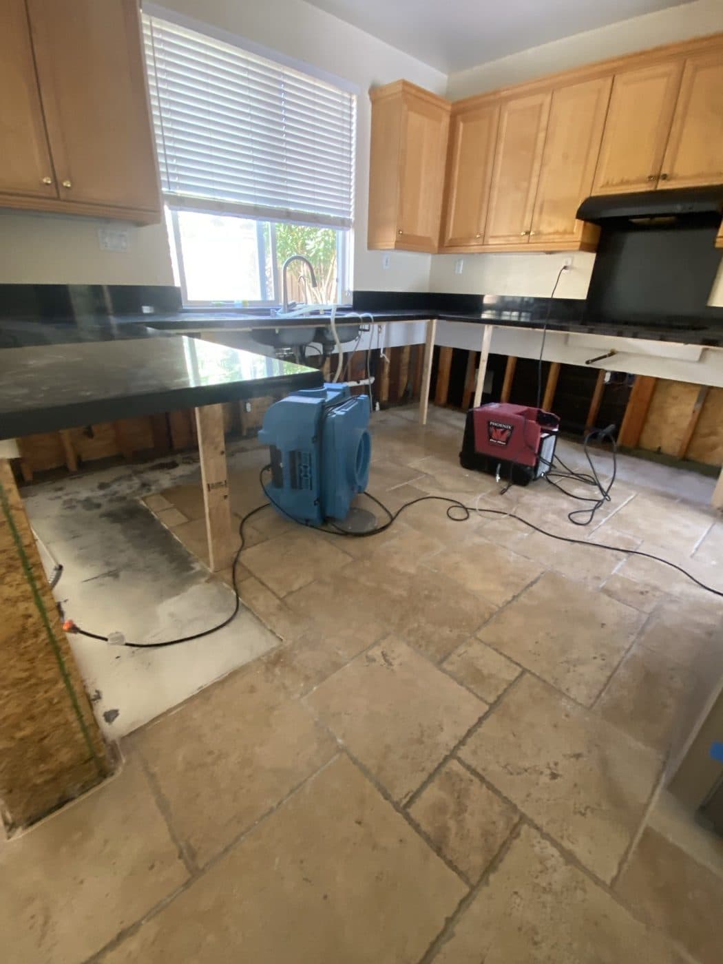 Industrial air movers and a dehumidifier drying a water-damaged kitchen